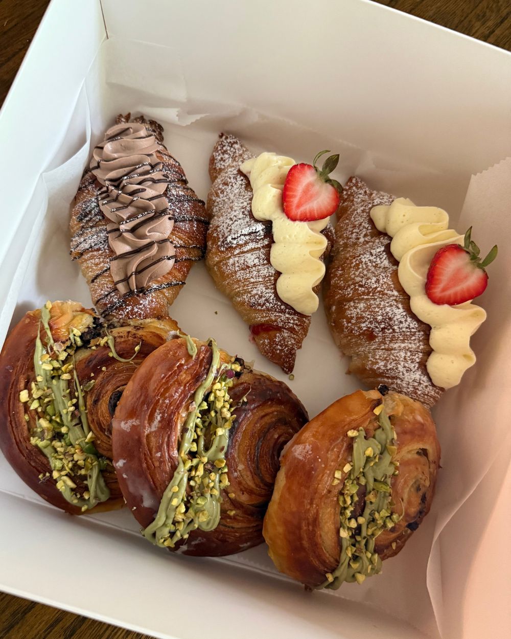 Box of strawberry, chocolate crémeux and pistachio croissants and escargots
