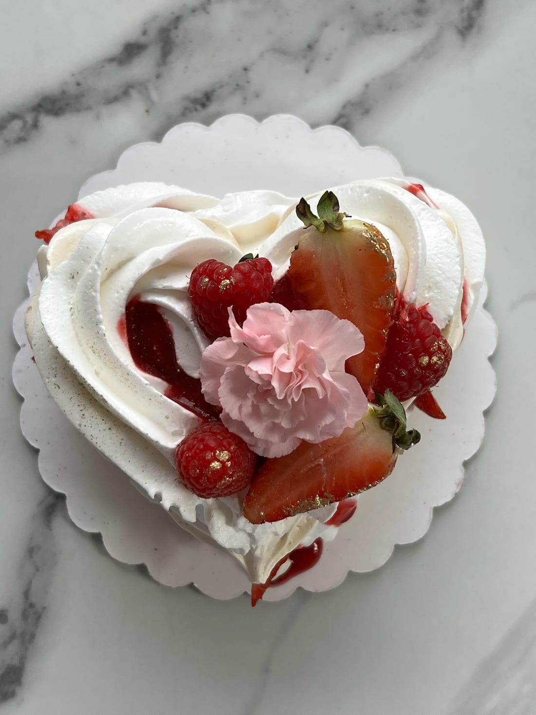Heart-shaped pavlova with strawberries, raspberries and a carnation