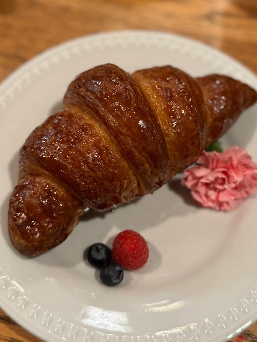 Glazed croissant on a plate with berries and a carnation