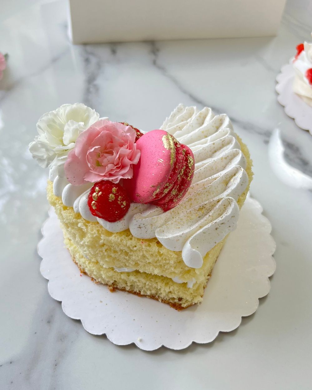 Heart-shaped layer cake with a pink macaron, raspberries and carnations