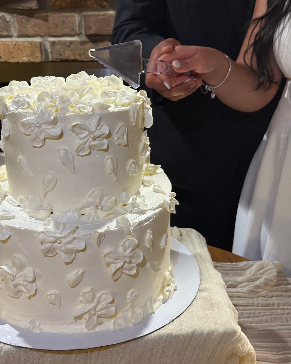 Two-tier white wedding cake with piped flowers being cut